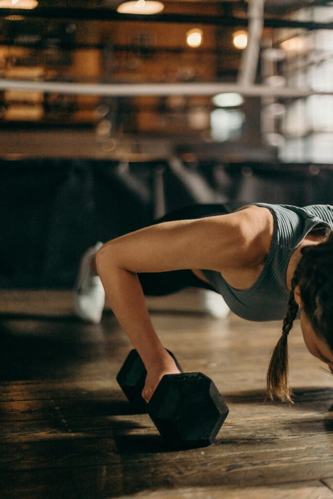 Woman doing push-up exercise using dumbbells on gym floor during strength training