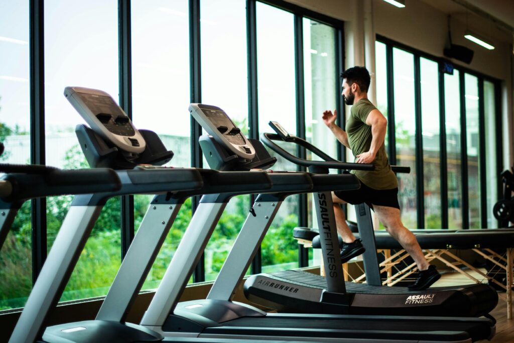 Man running on treadmill in a modern gym with large windows and fitness equipment